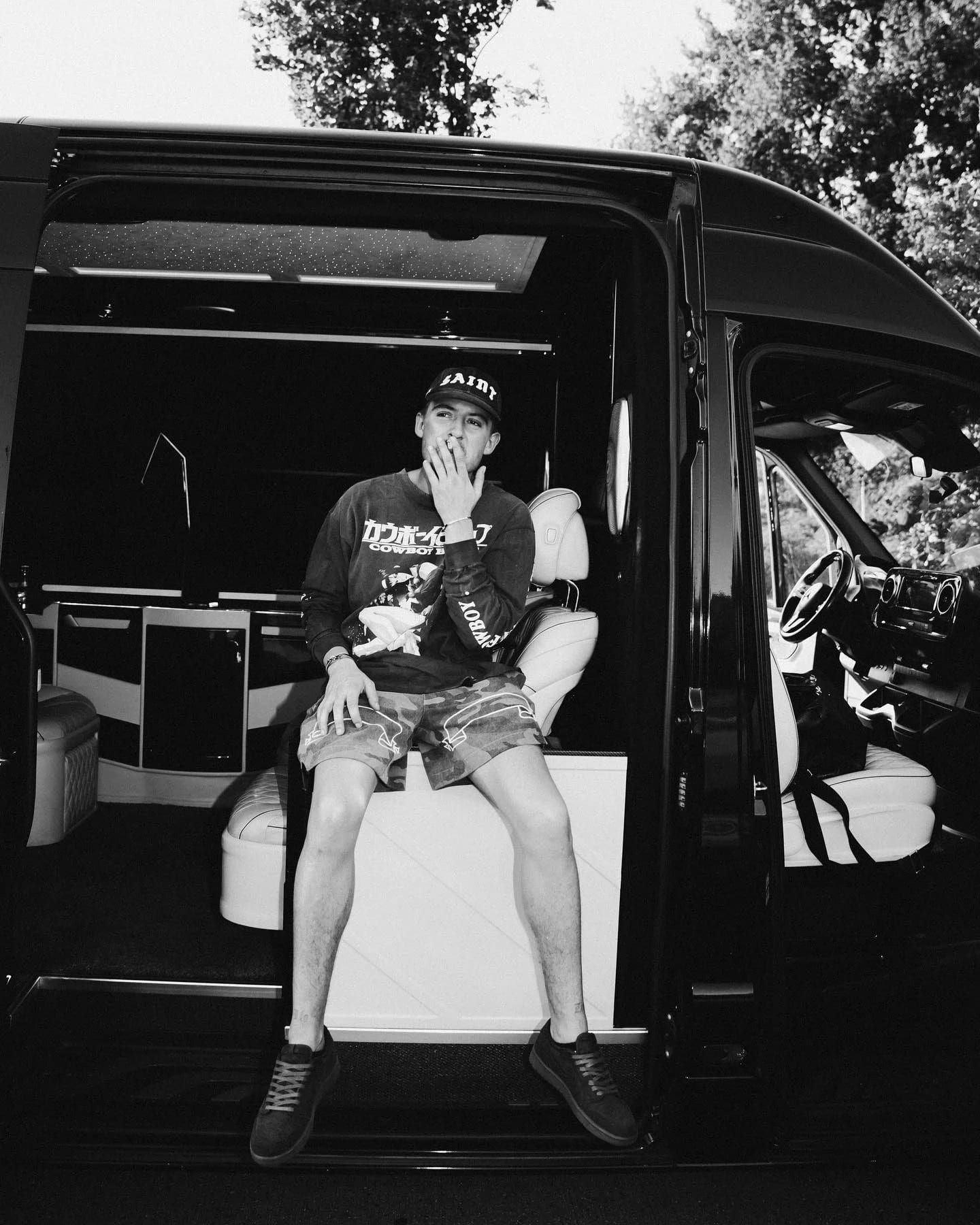 A person seated in a vehicle doorway, photographed in black and white